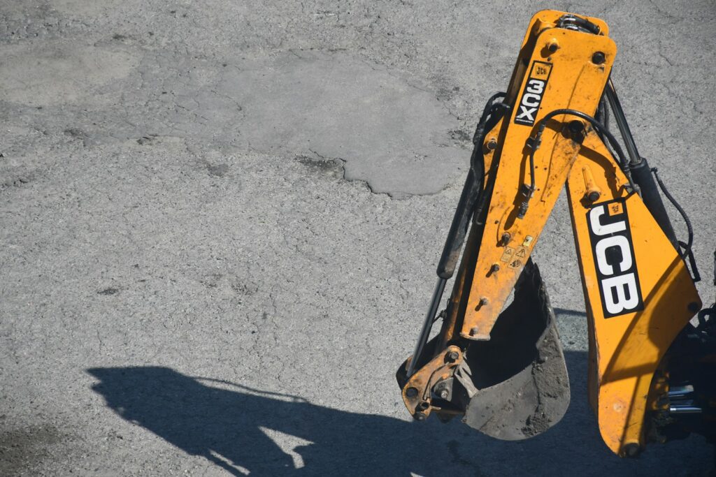 Yellow excavator arm and bucket casting shadow on ground